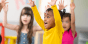 Young student participating in classroom activity by raising both hands up
