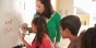 A teacher assisting students with a math equation on a whiteboard.