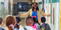 A school leader welcomes children in a hallway.