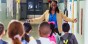 An educator smiles in front of a group of students in a school hallway.